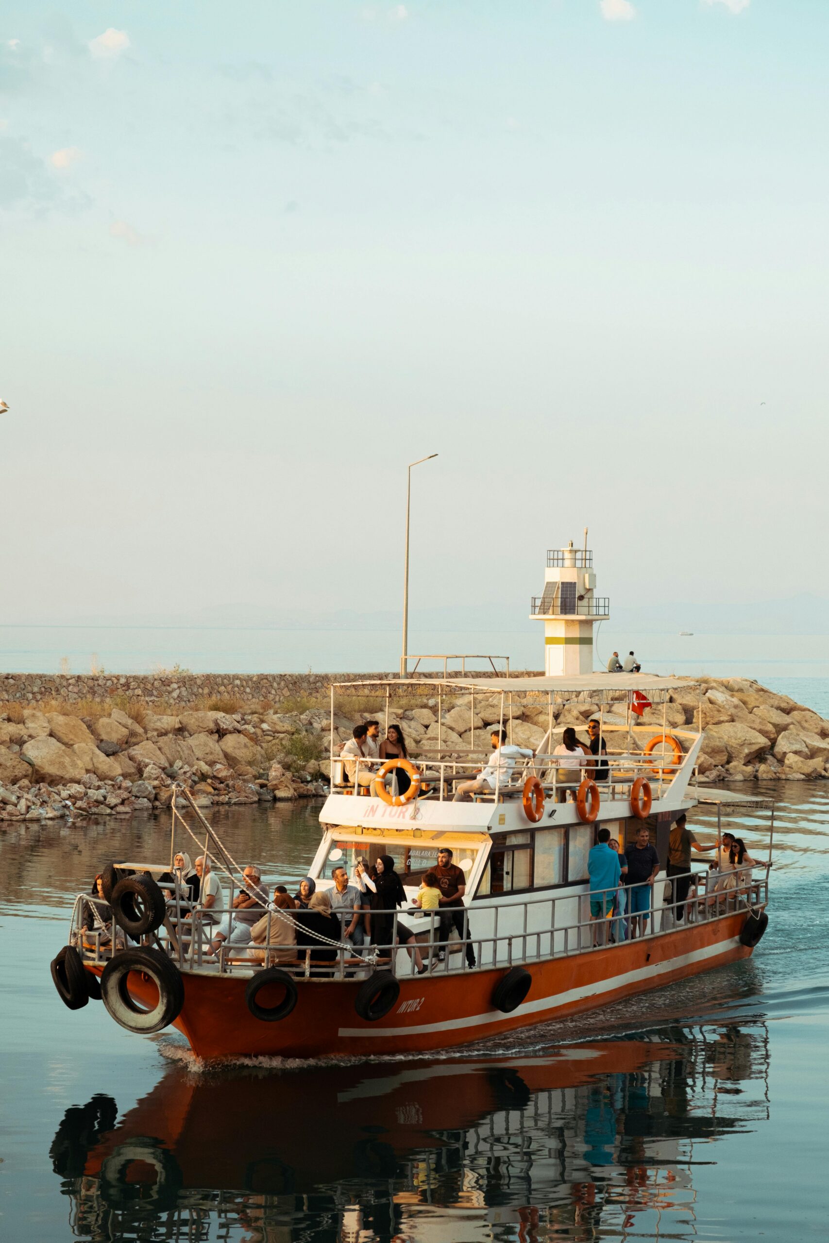 A boat with tourists near a coastal lighthouse during sunset, offering a scenic travel vibe.